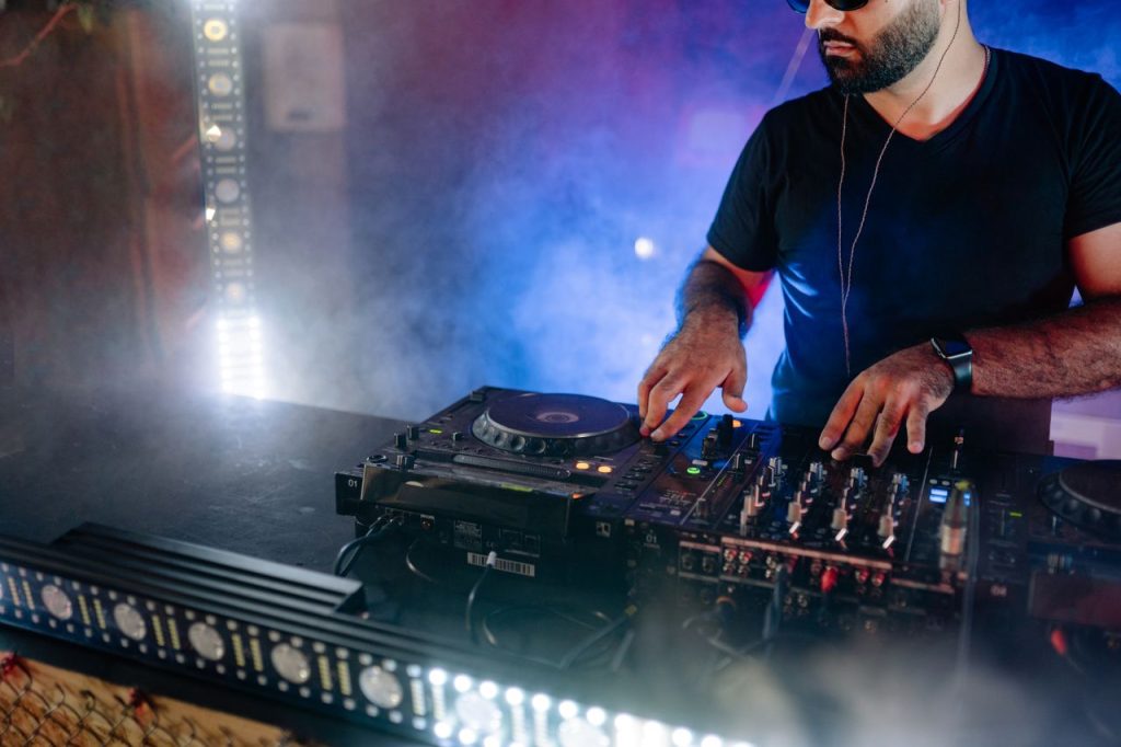 Energetic DJ performing live with mixing equipment in a colorful nightclub setting.